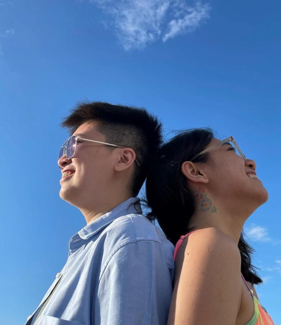 Lesbian couple posing back to back with the sky as background