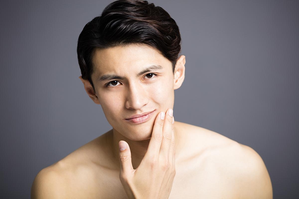 Handsome Asian man touching his face against gray background