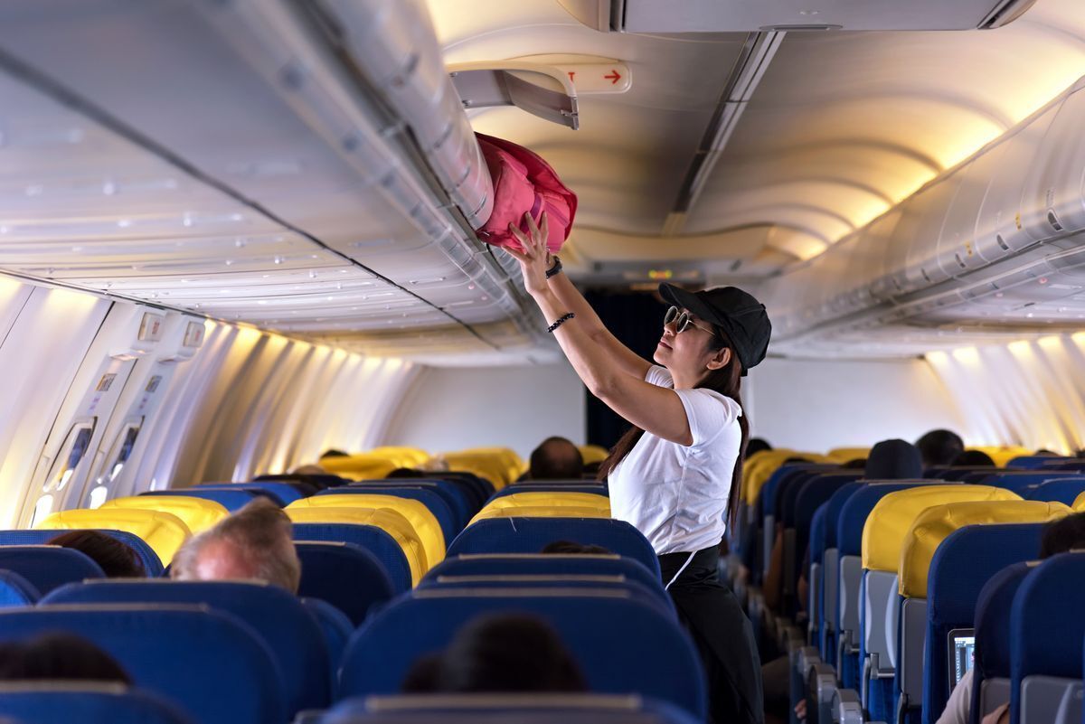 Asian woman putting luggage in the overhead compartment. 