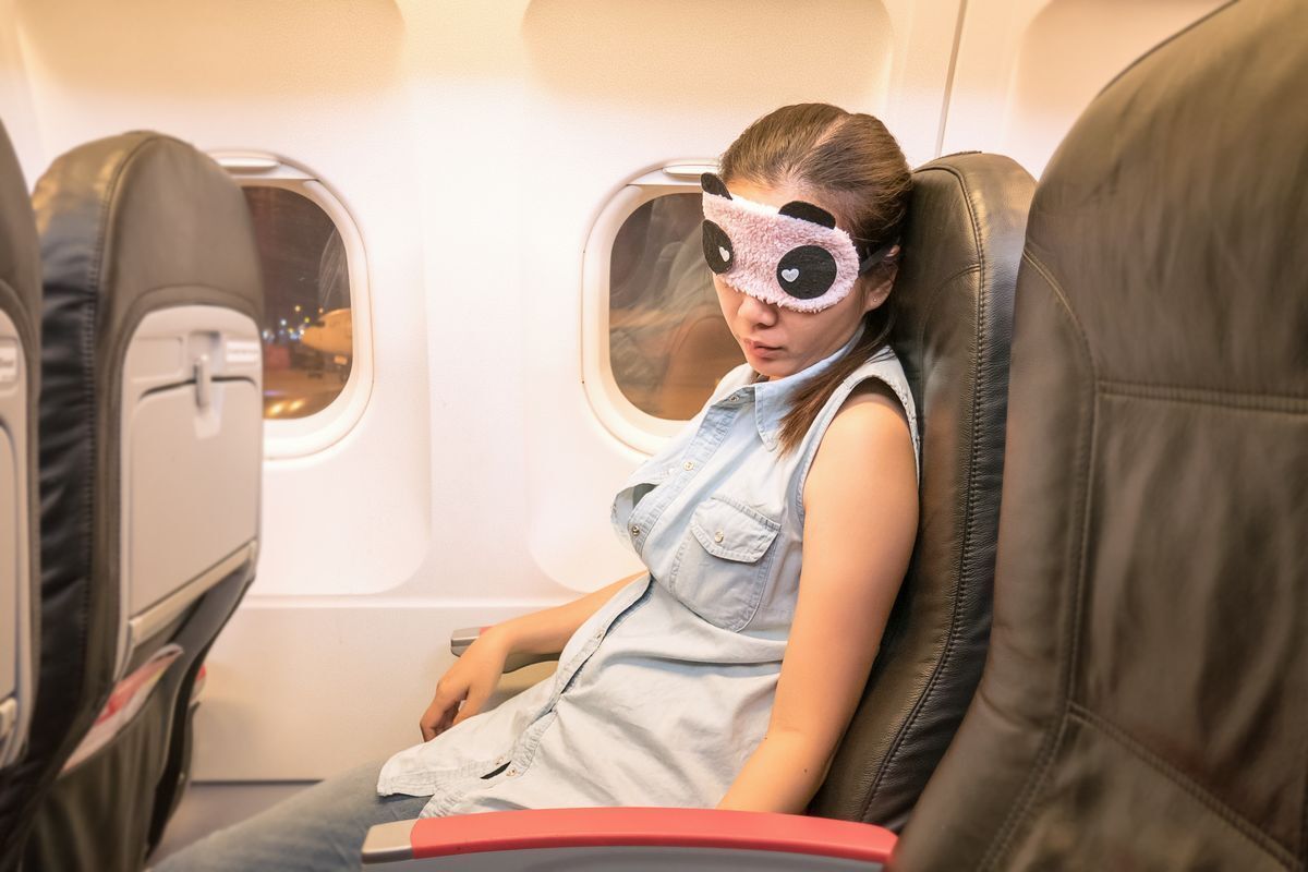 Asian woman with panda eye mask sleeping on a plane.