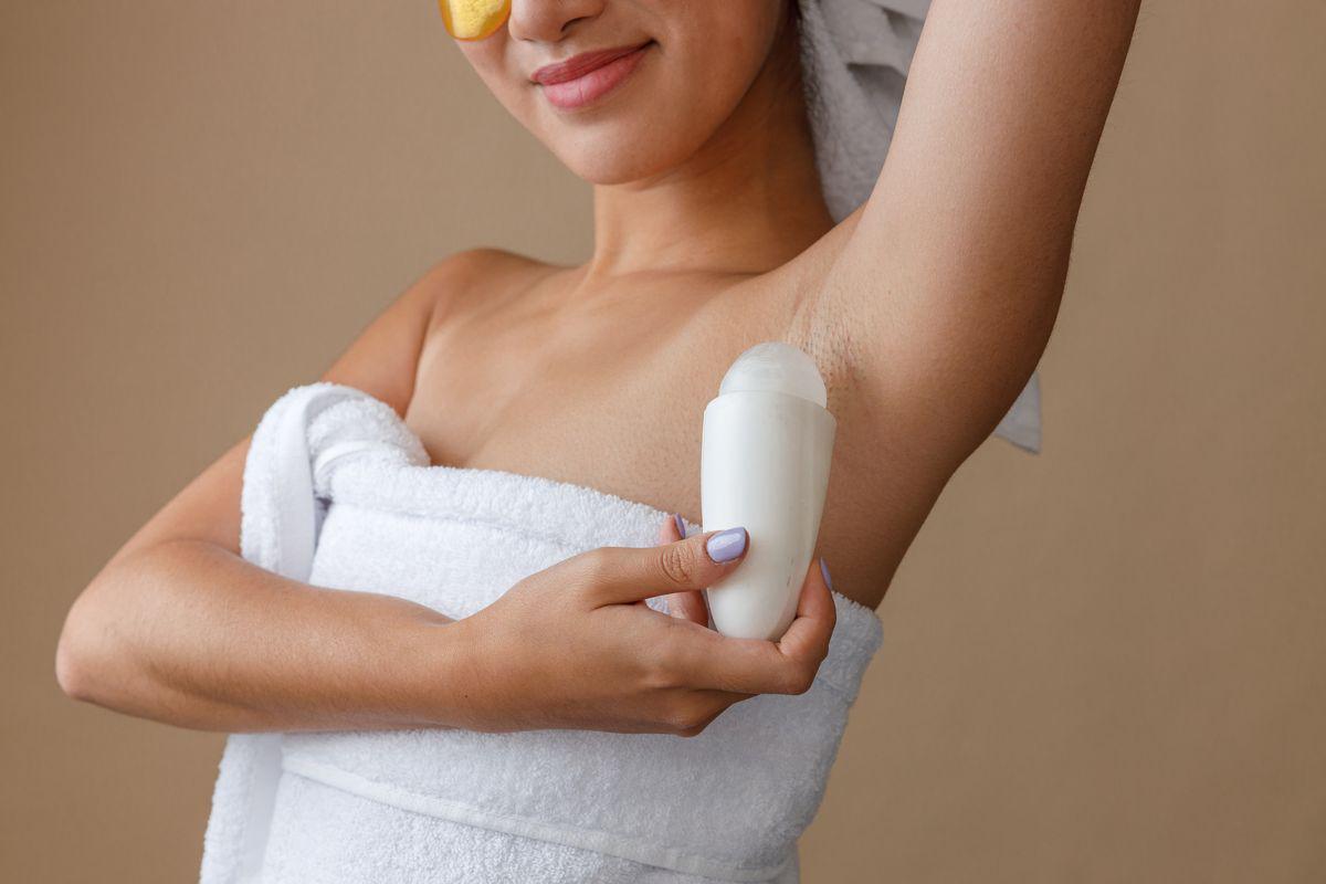 Woman in a white towel applying roll on deodorant 