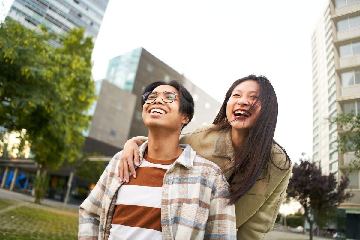 Man with glasses and woman with long hair laughing together outdoors.