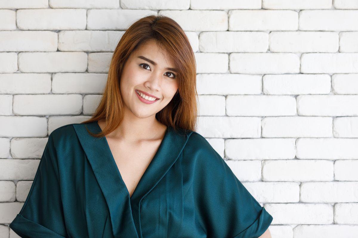 Smiling Asian woman against brick white wall 
