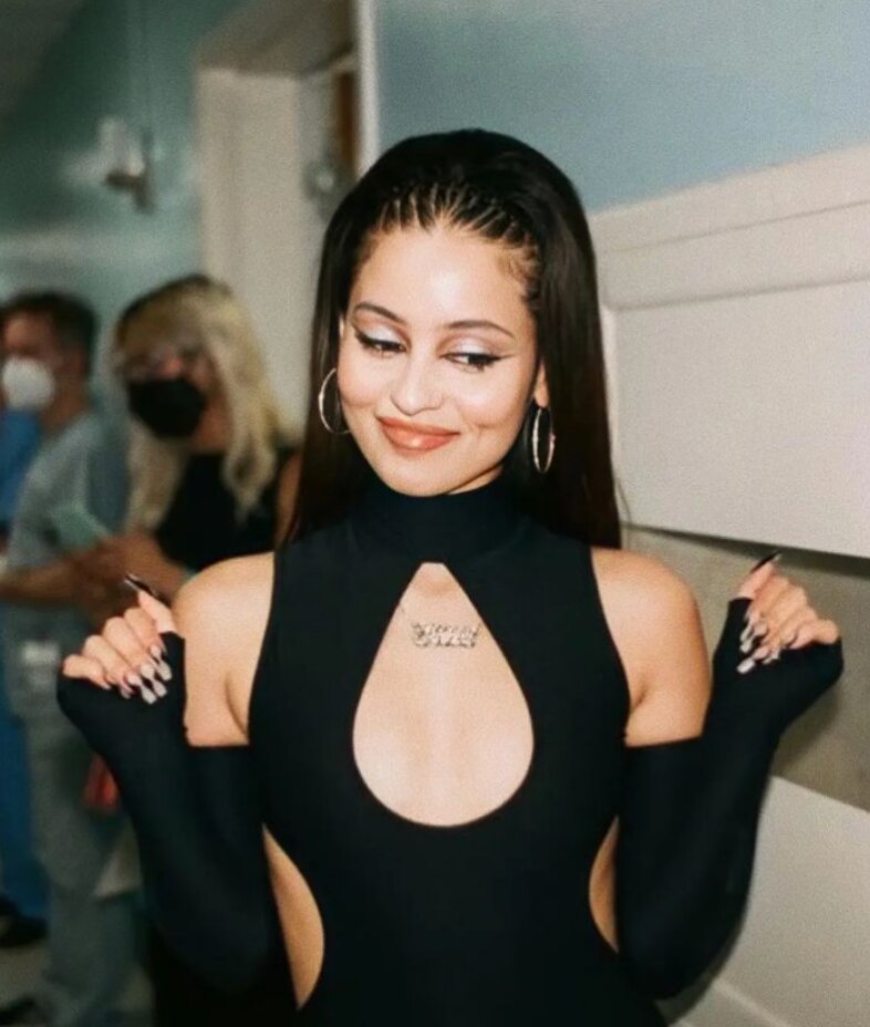 A woman in a black cut out dress, gold ear hoops, and zig zag comb headband. 