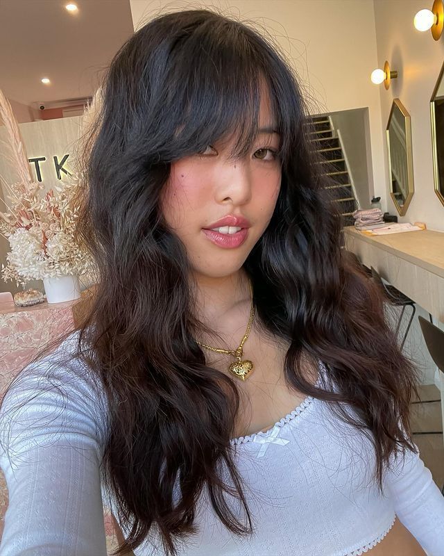 Woman with long curly hair and short curtain bangs.