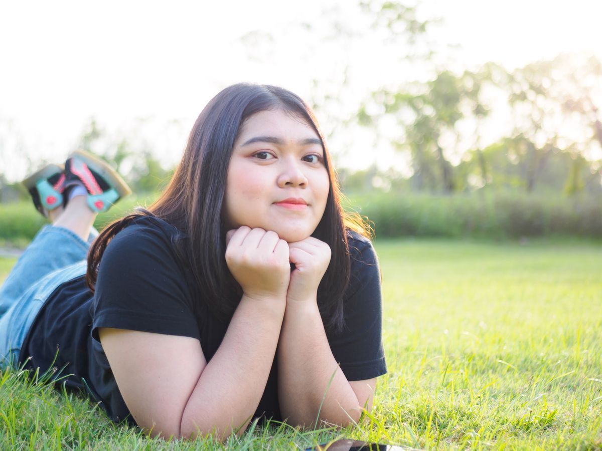 Woman with chubby cheeks laying on top of grass.
