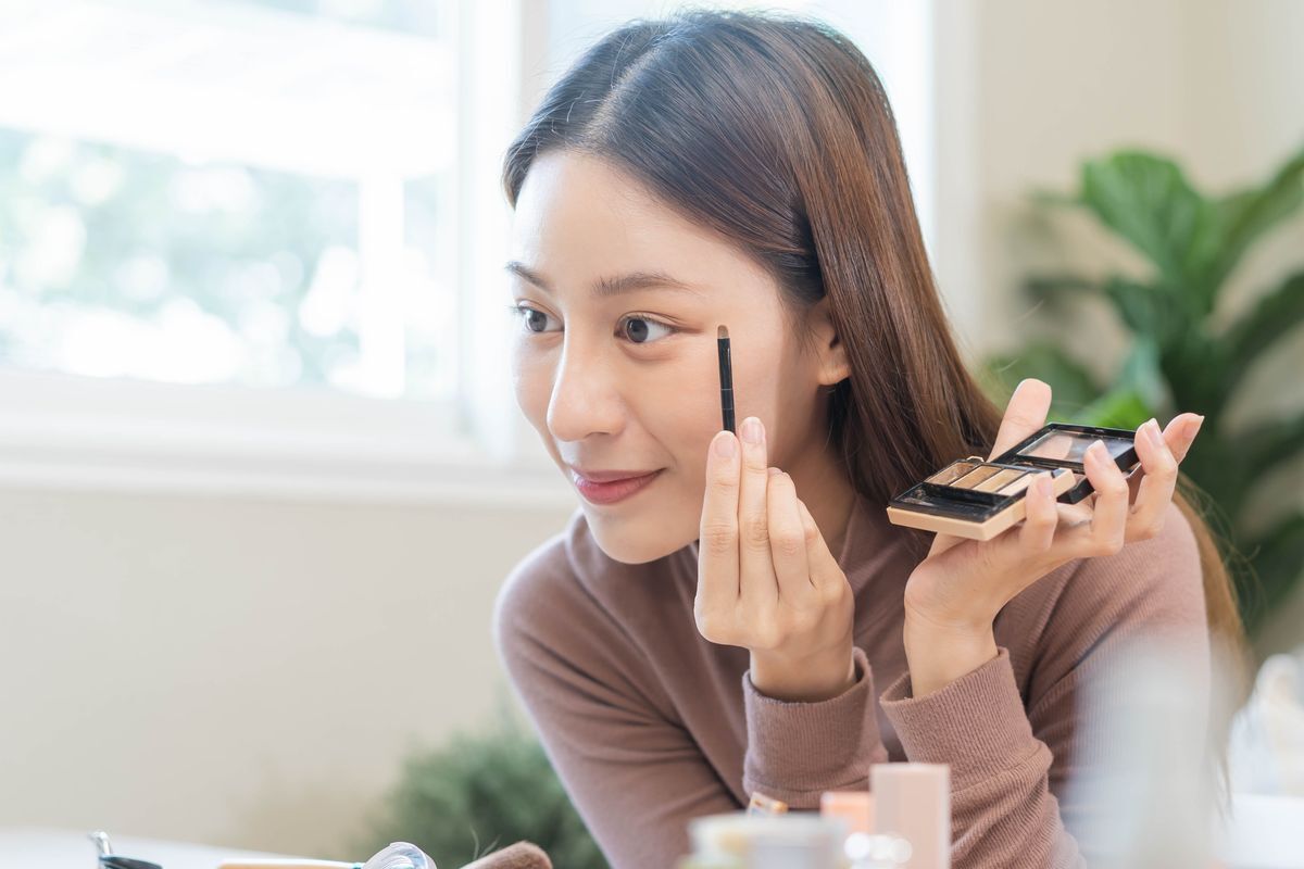 Woman applying eyeshadow to her eyelid with a small brush.