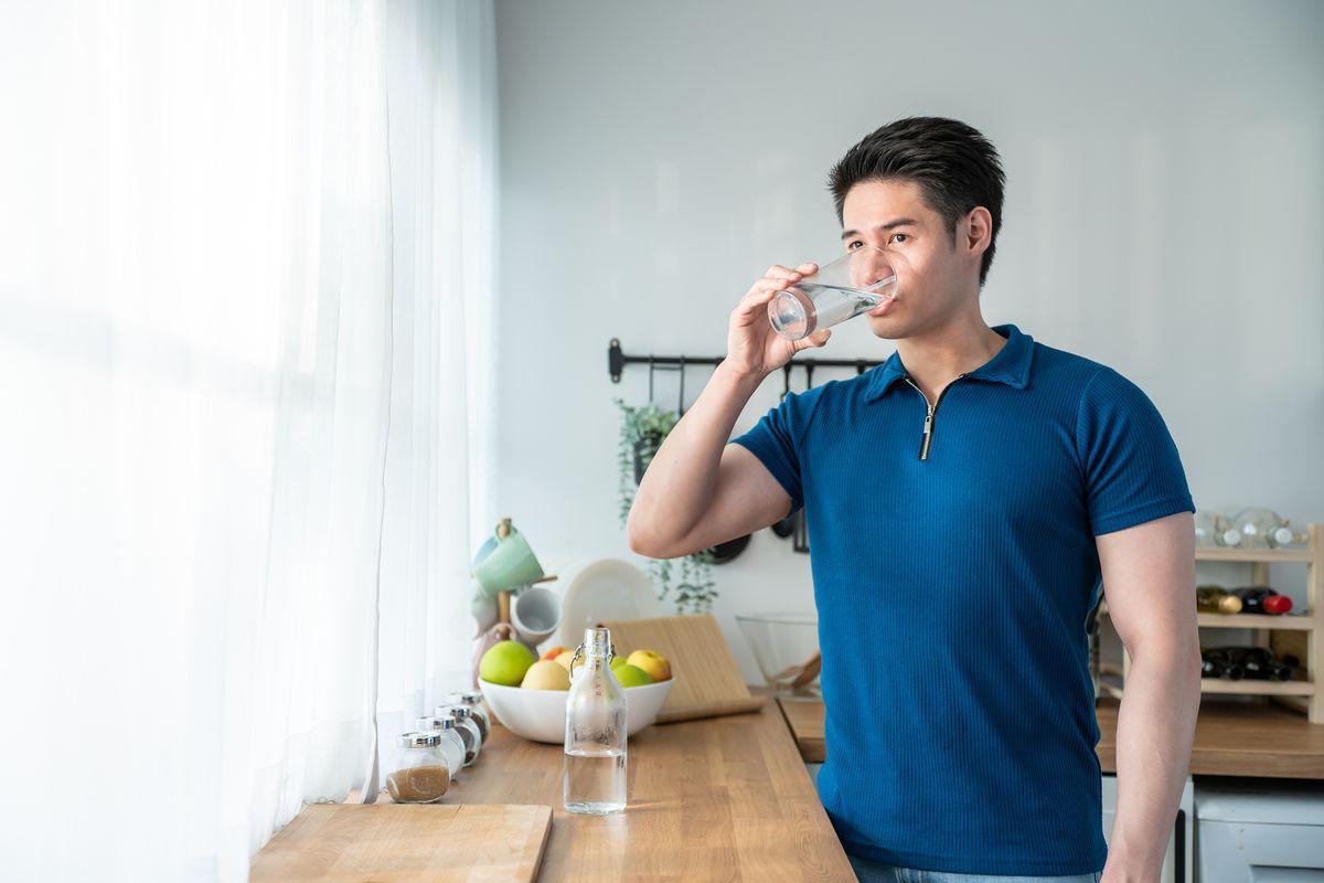 Asian man drinking water in kitchen