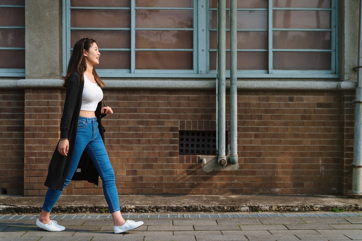Woman in white cropped top and jeans walking outside.