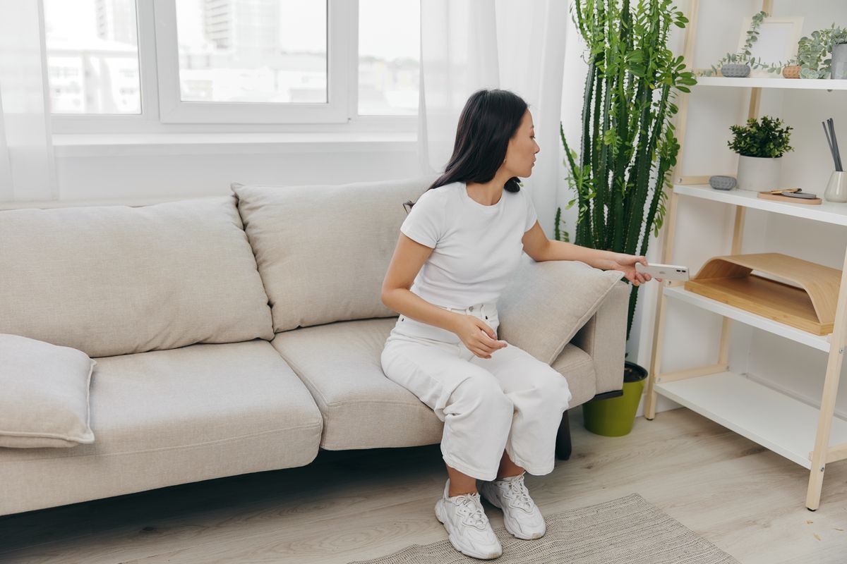 Asian woman sitting on sofa putting phone away.