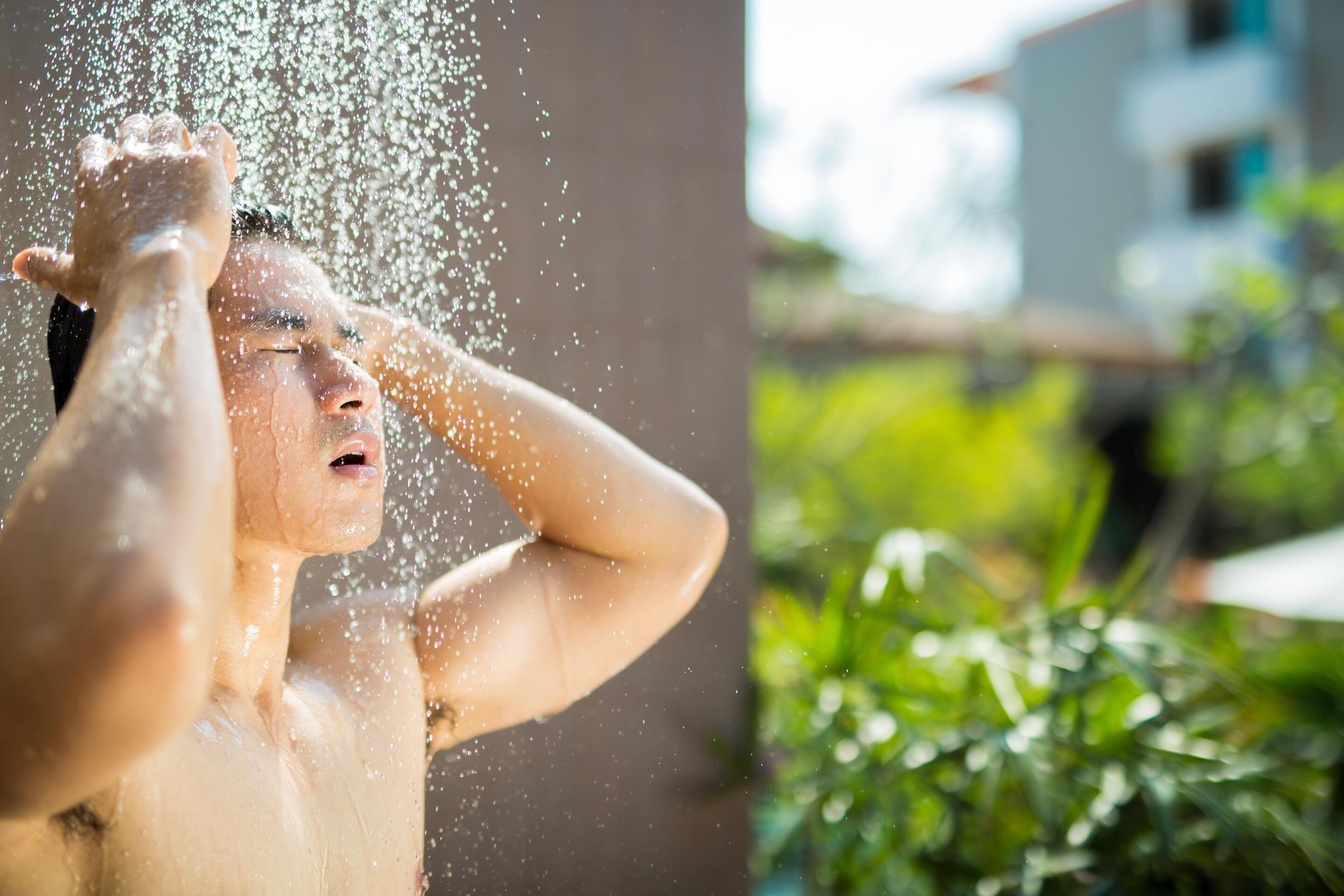 A young man takes an outdoor shower while traveling.