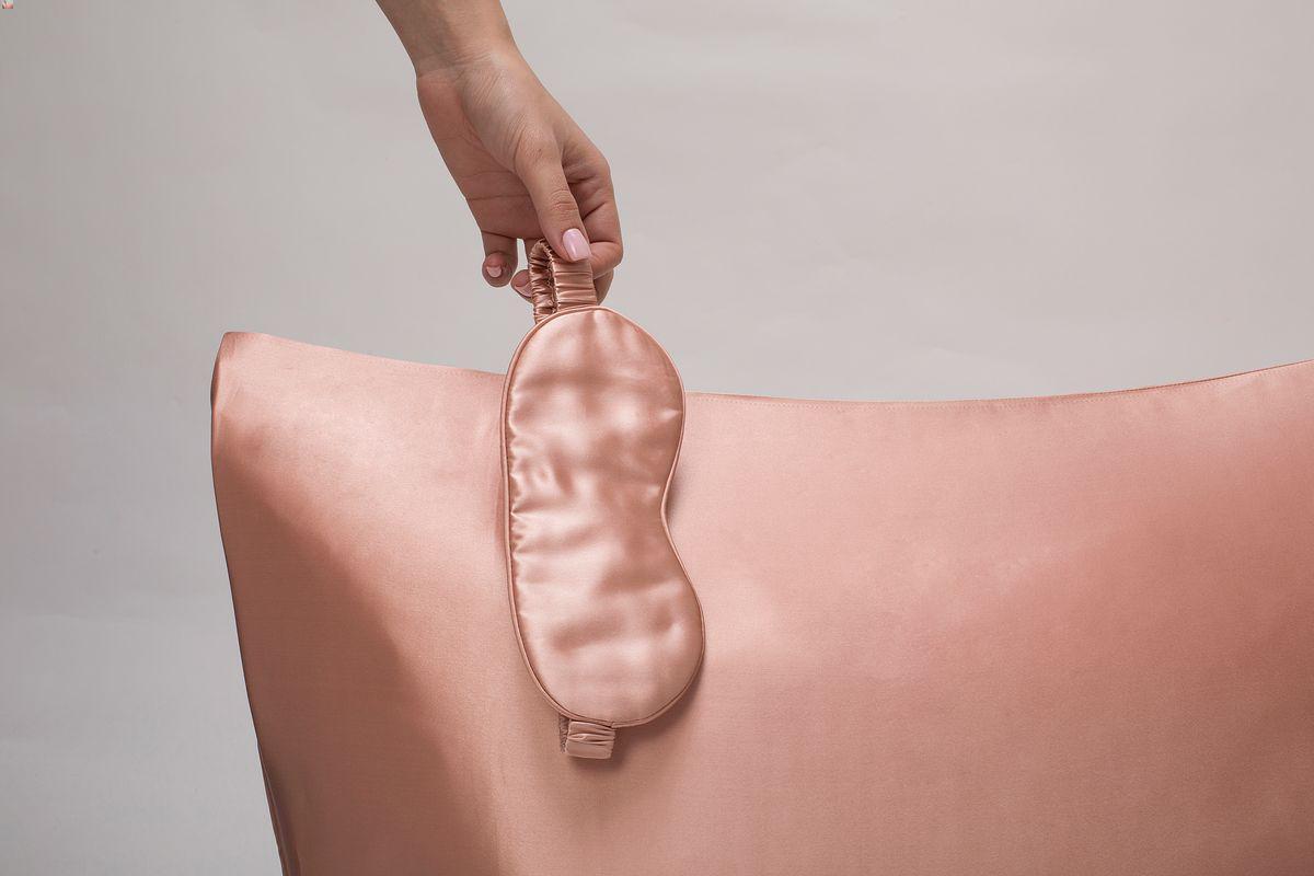 Woman holding a sleep mask over a silk pillow