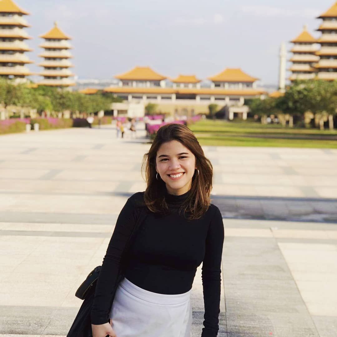 An Asian woman in a black turtleneck posing in front of pagodas