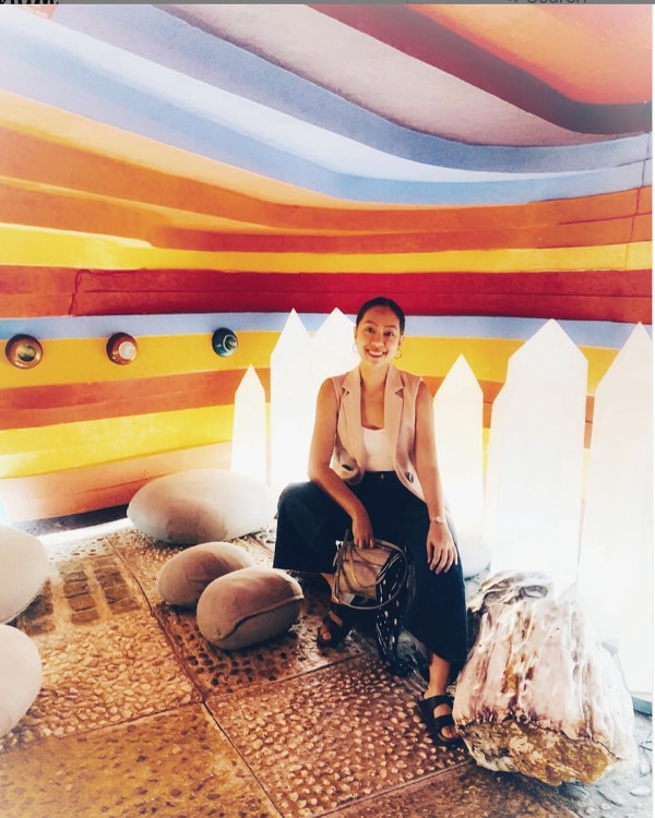 A woman in black pants and beige vest posing at an art show
