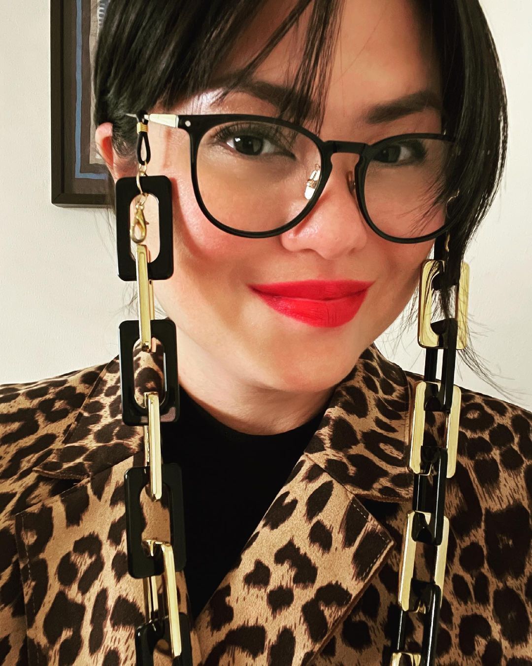 A woman in a cheetah print jacket, spectacles with chunky chains, and red lipstick