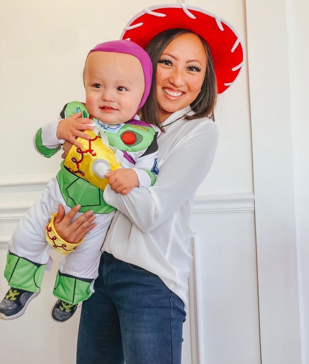 Woman wearing red hat and baby in a Buzz Lightyear costume.