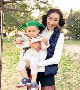 Woman dressed up as Princess Leia holding her baby who is wearing Yoda hat.