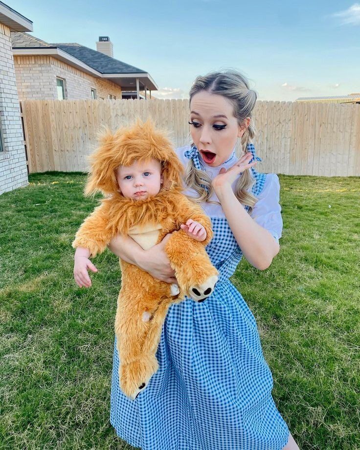 Woman wearing blue gingham dress posing with a baby in a lion suit.