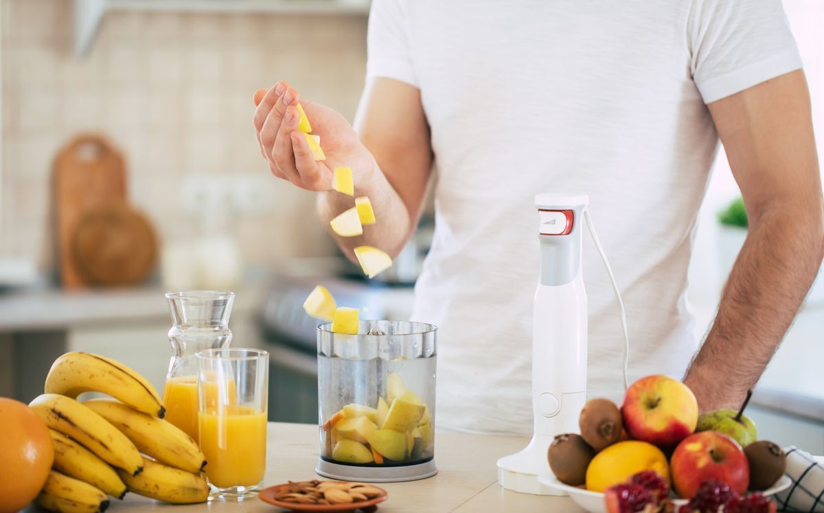 A man making a smoothie in a blender with fruits and juices.