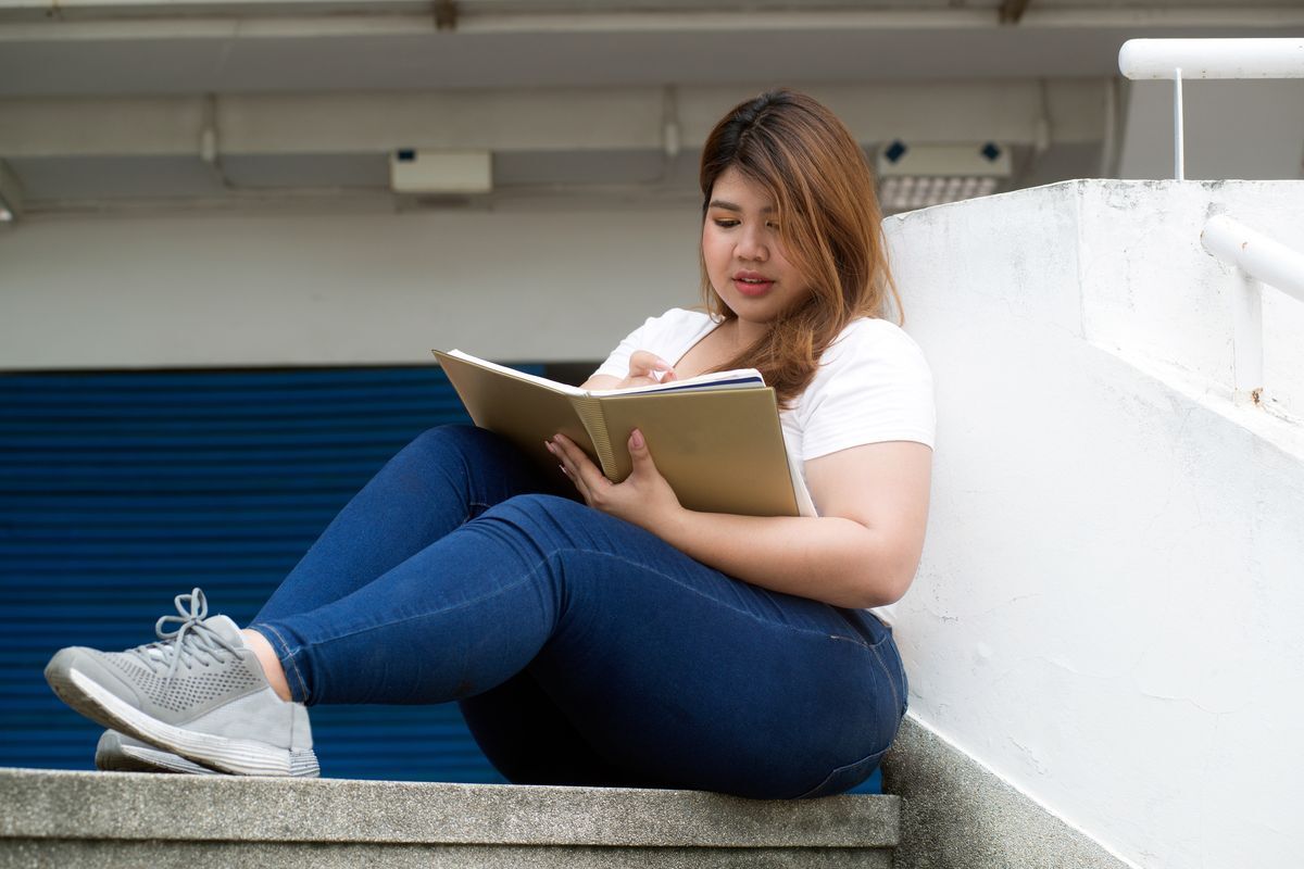 Filipino woman seated on steps reading a book.