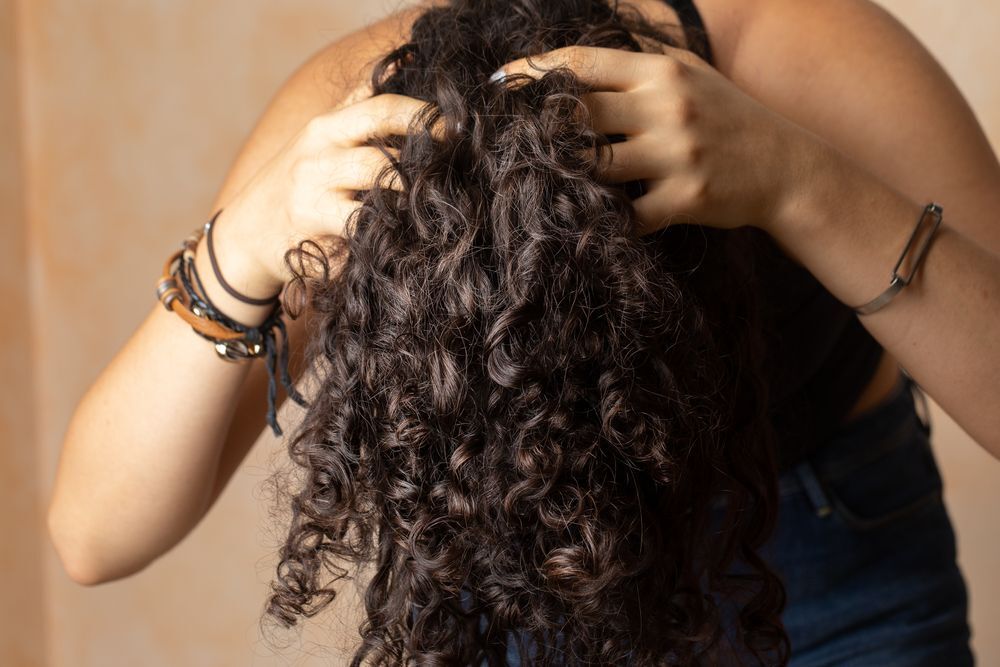 Woman with curly hair massaging her scalp with her fingers.