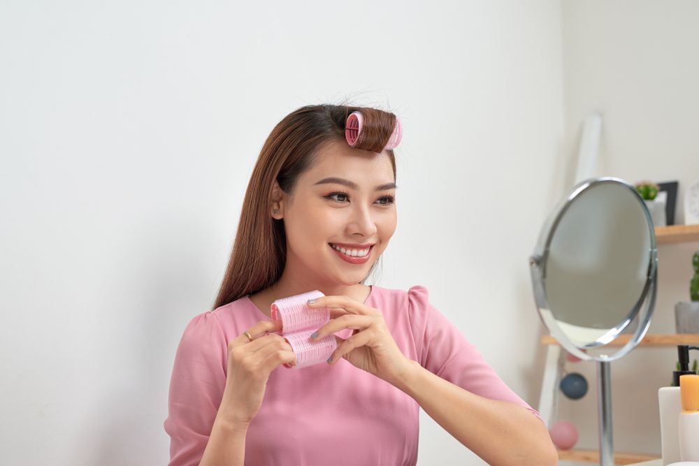 Woman with pink hair roller on the front of her hair holding more hair rollers.