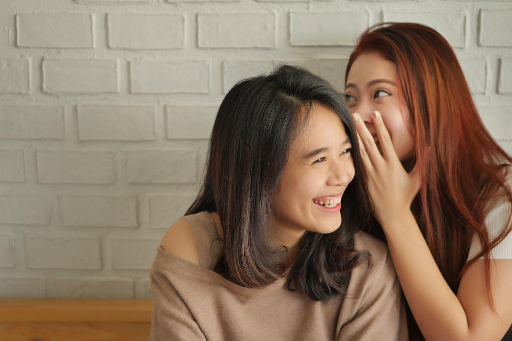 Asian friends whispering and laughing