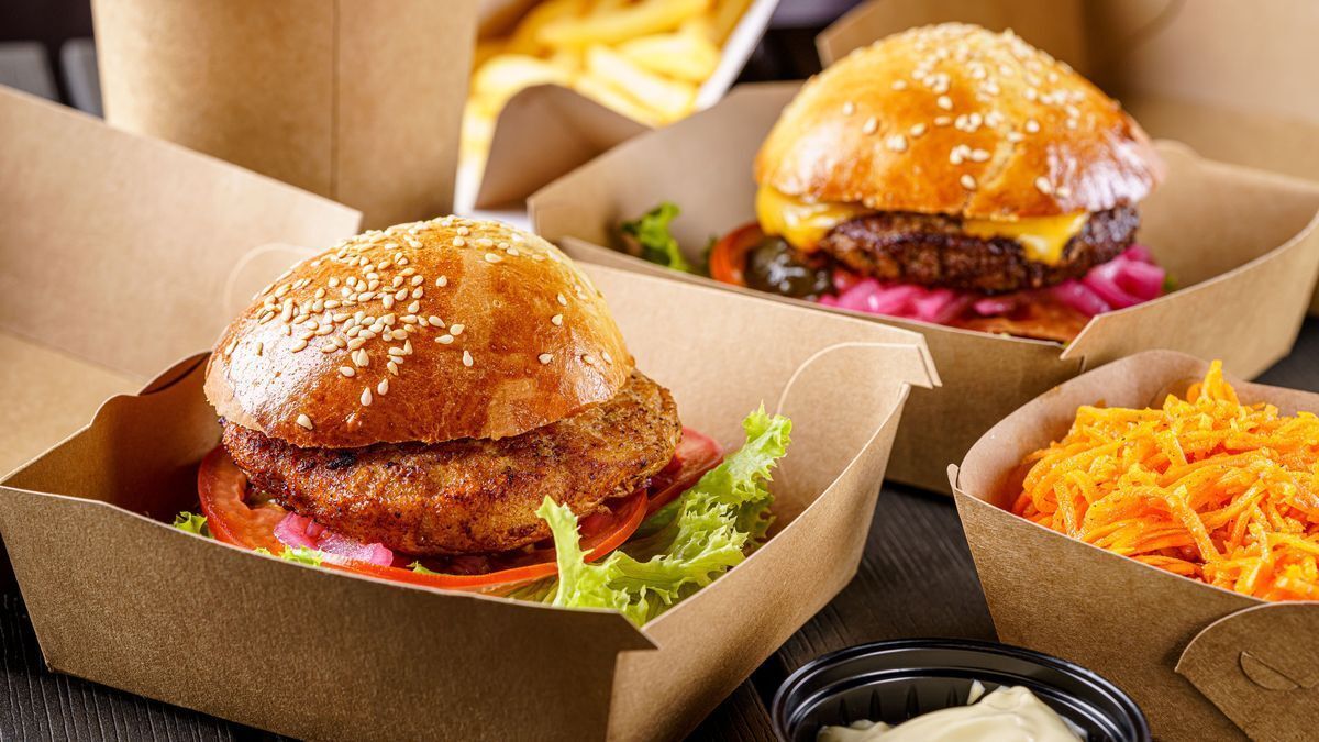 Different burgers with fries and other sides in folding paper burger boxes.