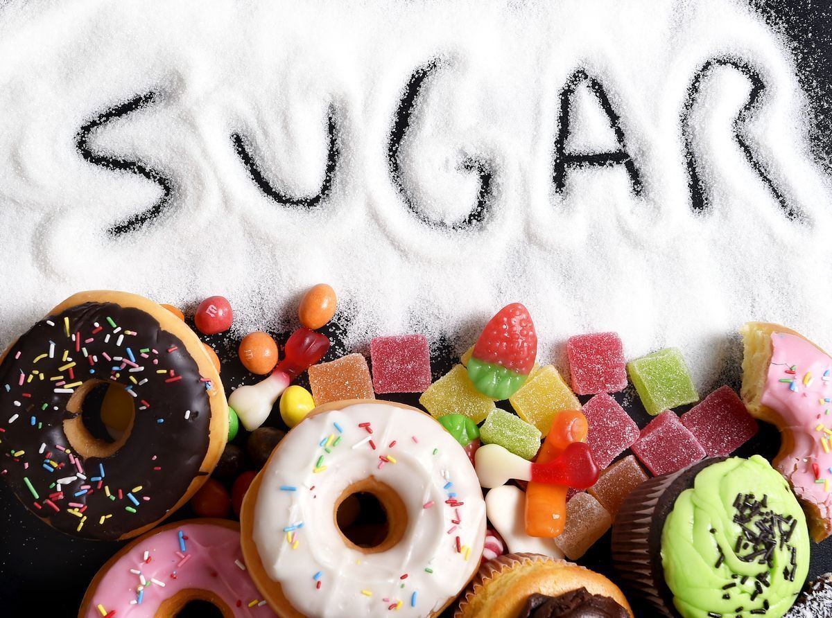 Sugar written out by a finger alongside donuts, candy, gummies, and cupcakes.