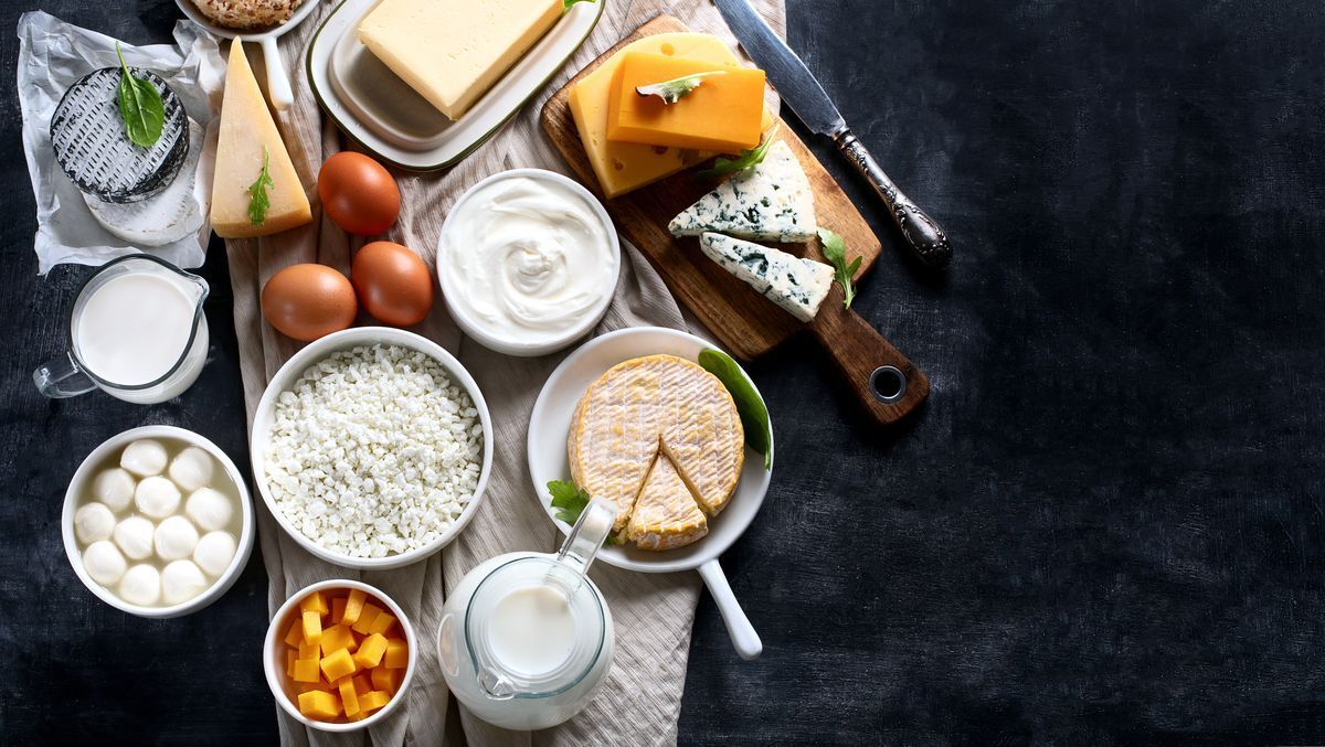 A flat lay of different kinds of dairy such as milk, sour cream, butter, and an assortment of cheese on a black tabletop
