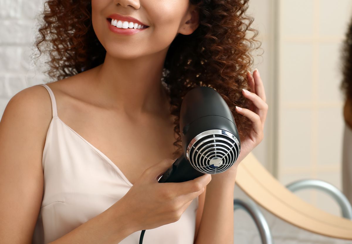 Woman using a hairdryer to dry her curly hair.