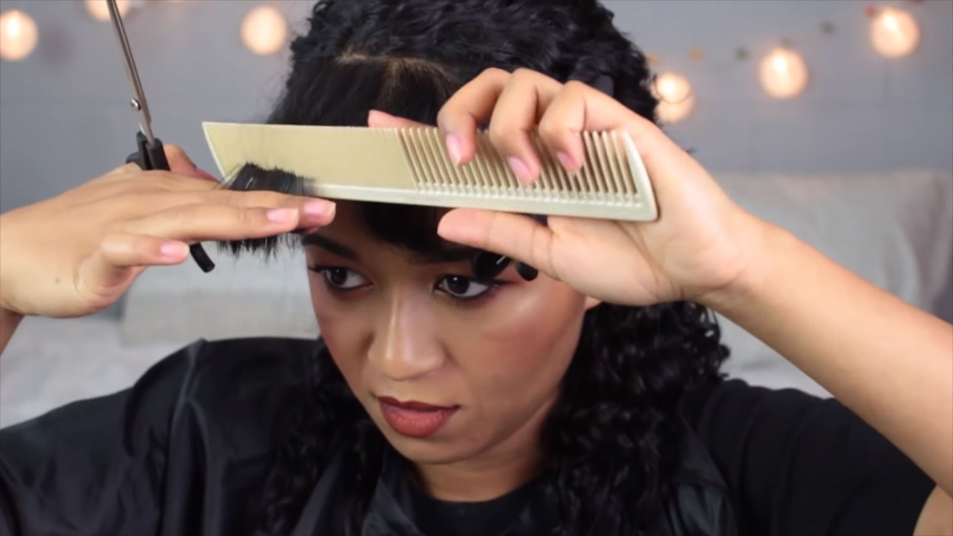 Woman brushing her bangs with a comb while holding a pair of scissors.