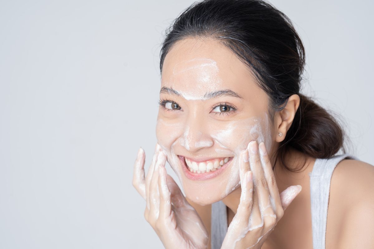 Young Asian woman happily washing her face against a white background.