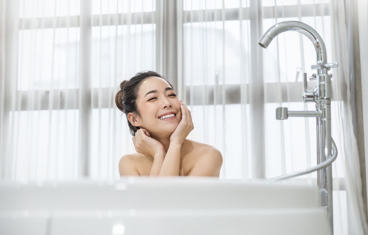 Asian woman smiling in the bathtub and resting her head on her hands.