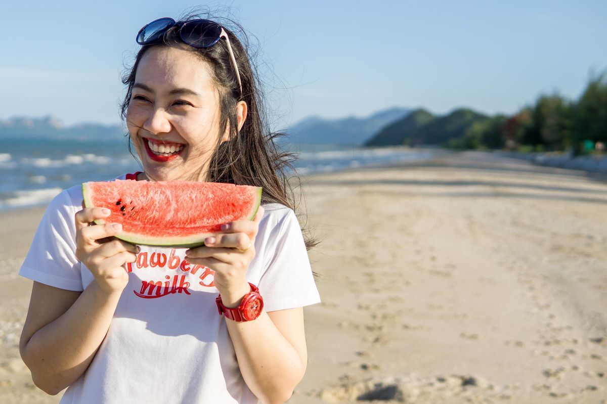 A woman holding a watermelon on a beach. 