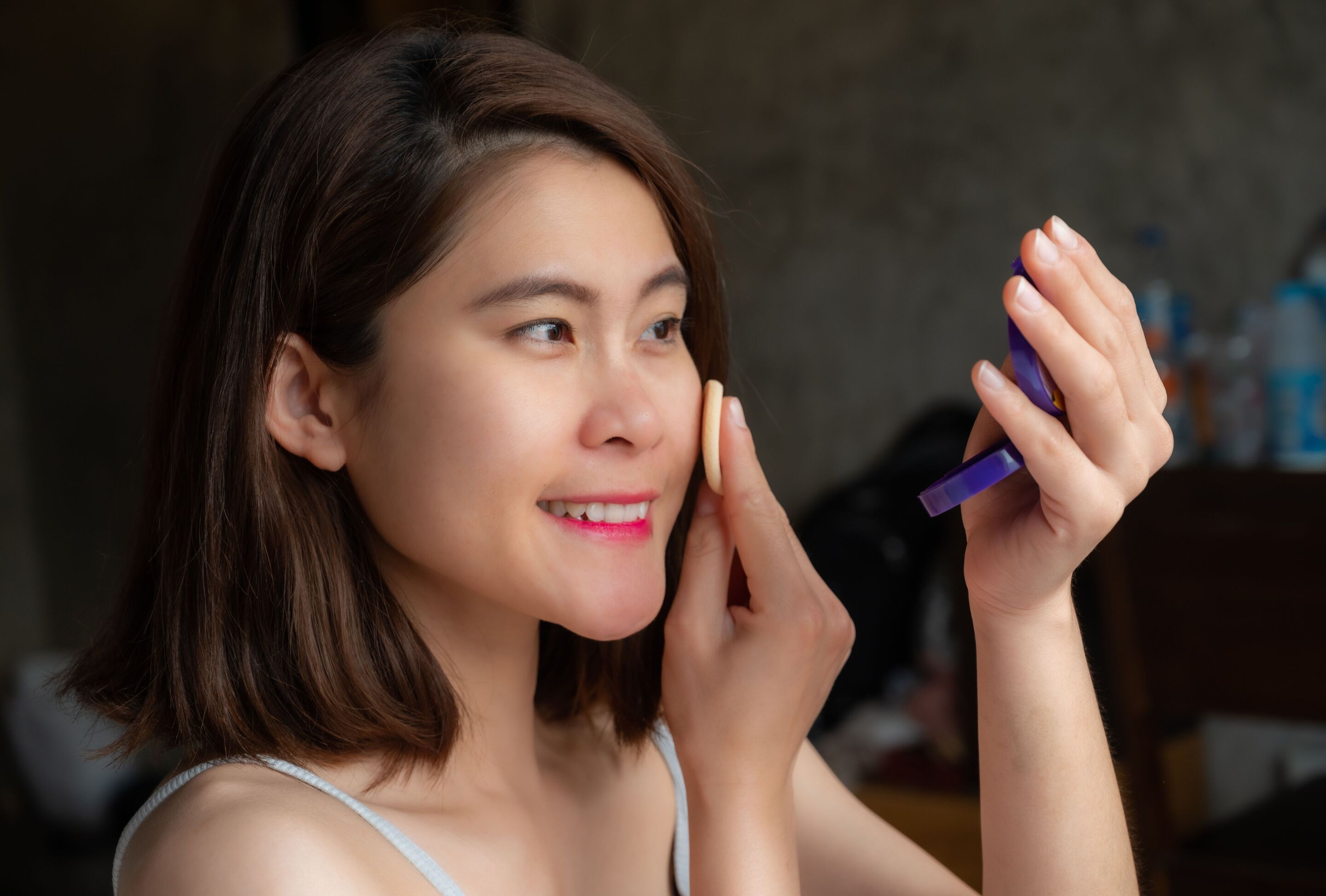 Asian woman applying powder foundation with a sponge.