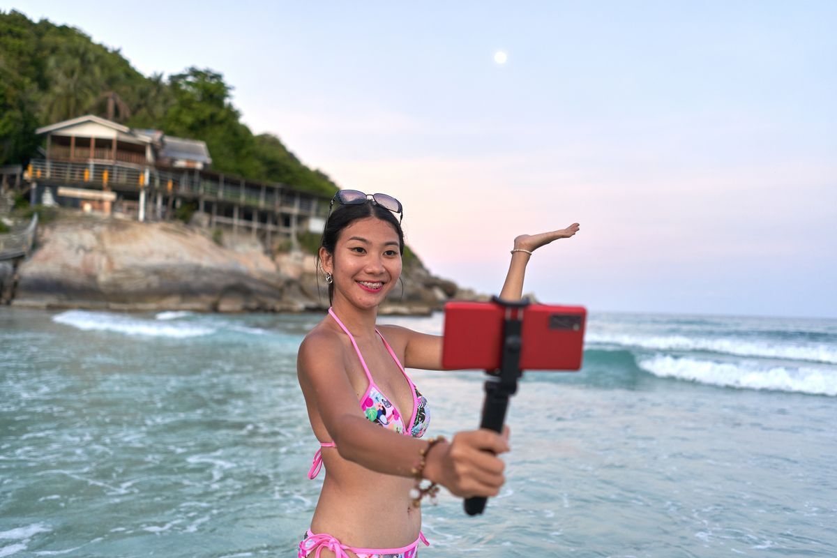 Asian woman taking a selfie at the beach with the moon in the background.