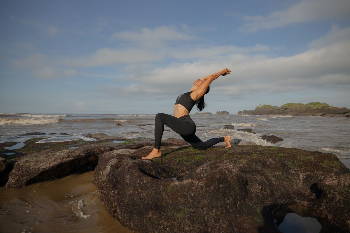 Asian woman doing yoga on top of rocks by the water.