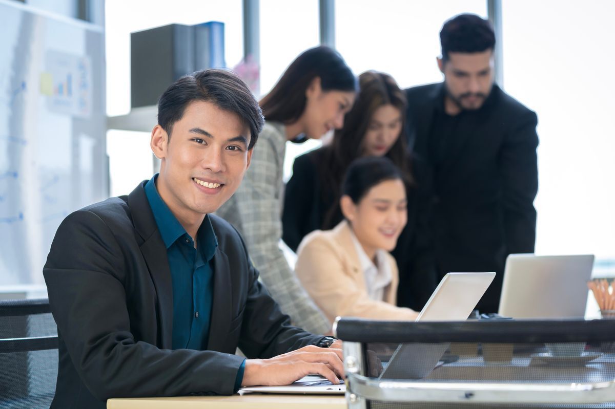 Smiling Asian man with his co workers behind him