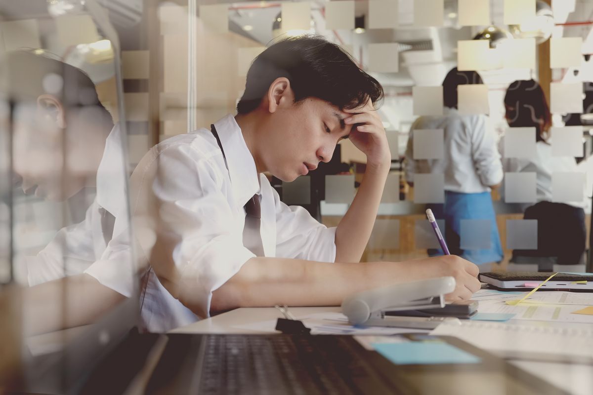 Asian man looking stressed while writing notes.