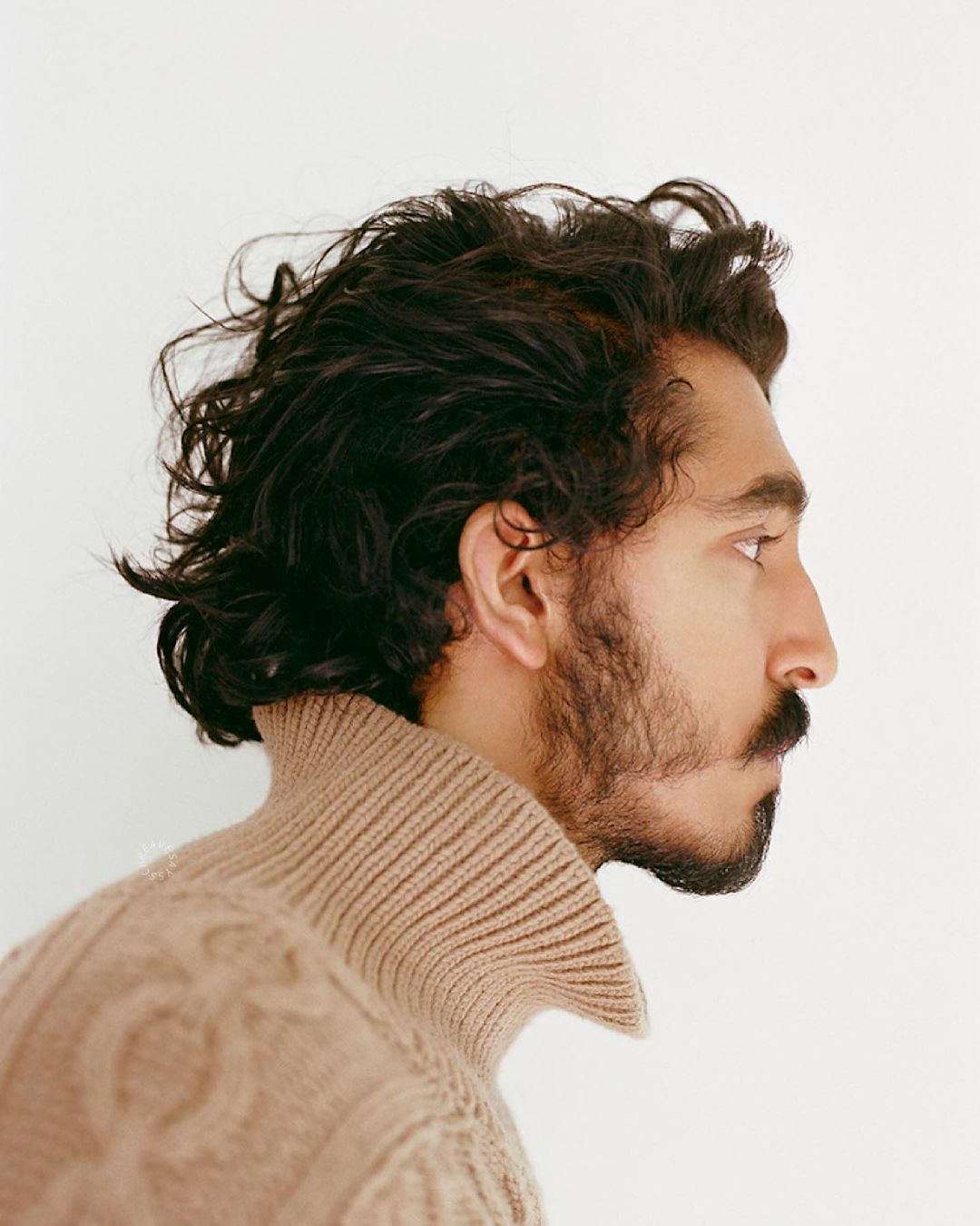 Dev Patel with curly hair and beige turtleneck.