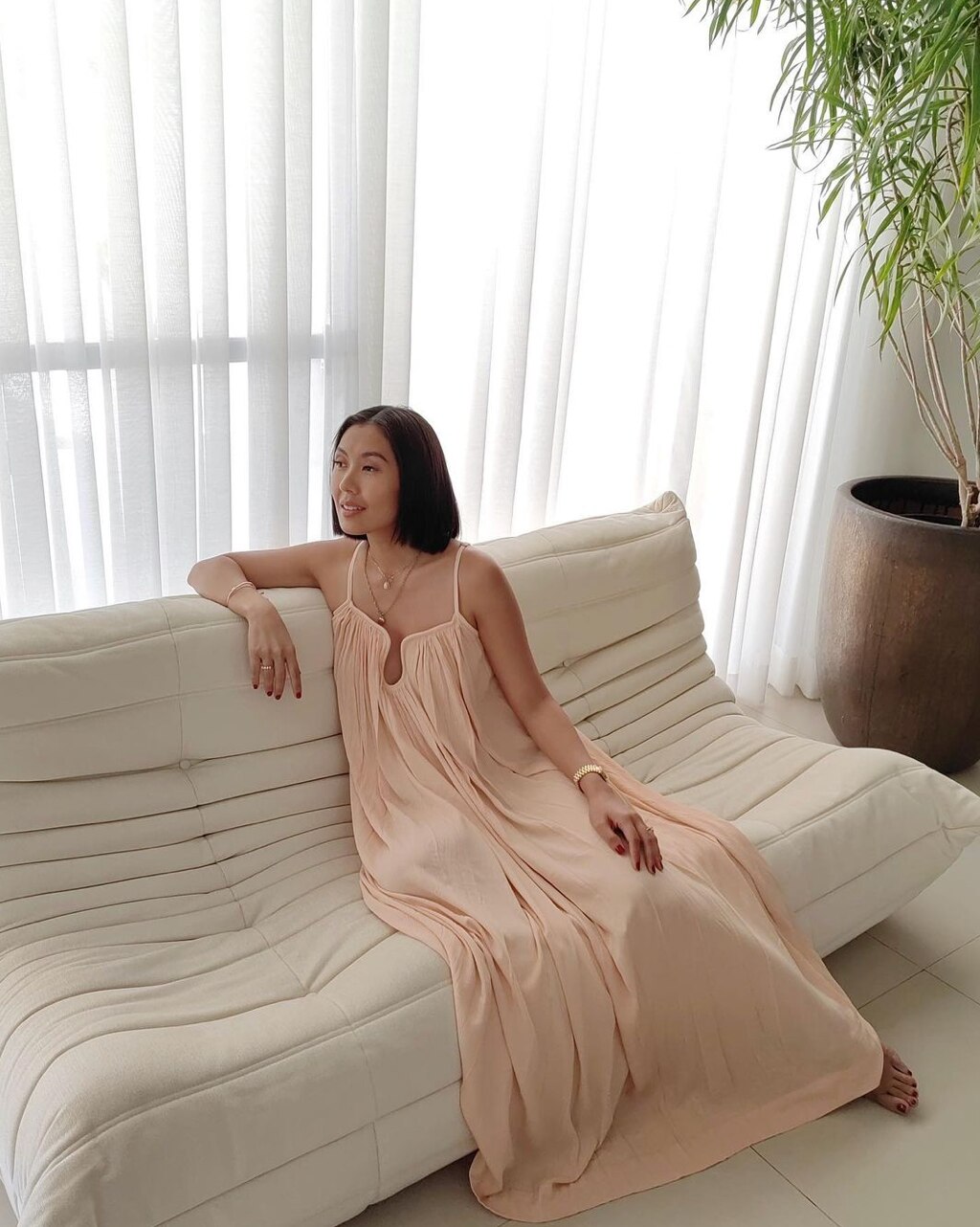 Asian woman wearing a maxi dress seated on sofa