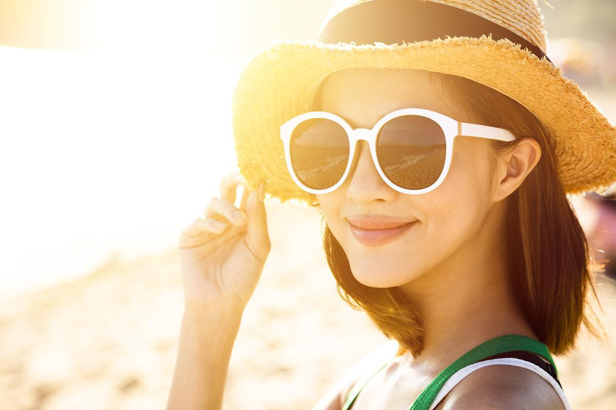 Asian woman wearing a hat and sunglasses at the beach