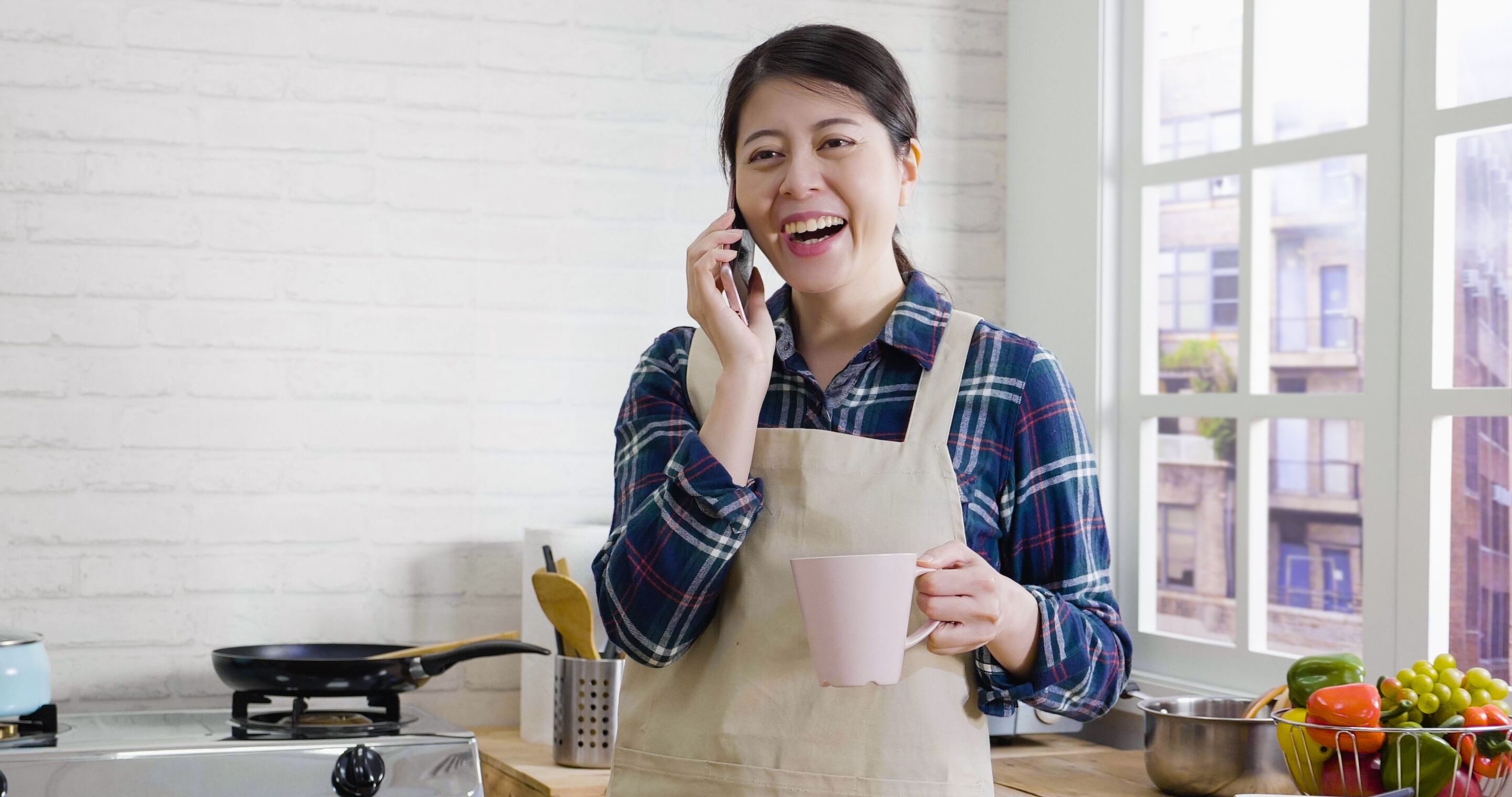 Asian mom taking a break in the kitchen while having coffee and talking on the phone