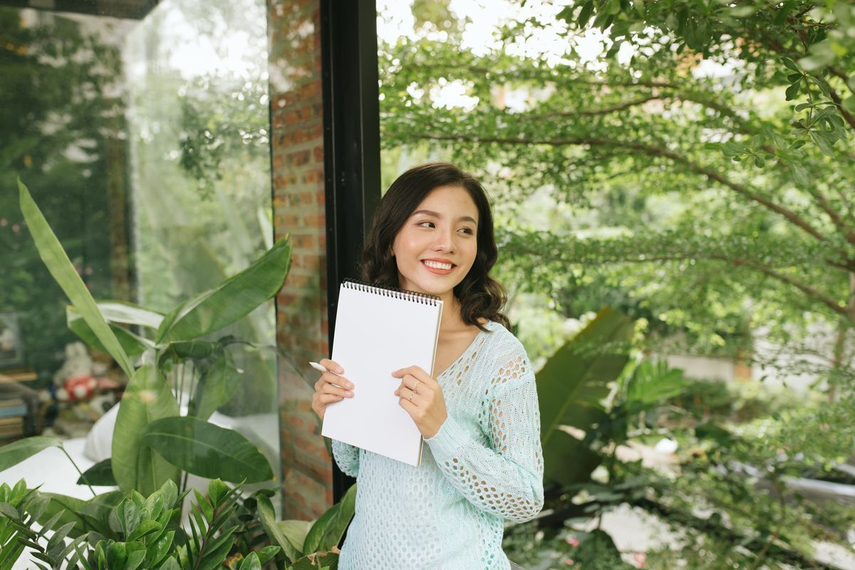 Asian woman holding a notebook while surrounded by plants