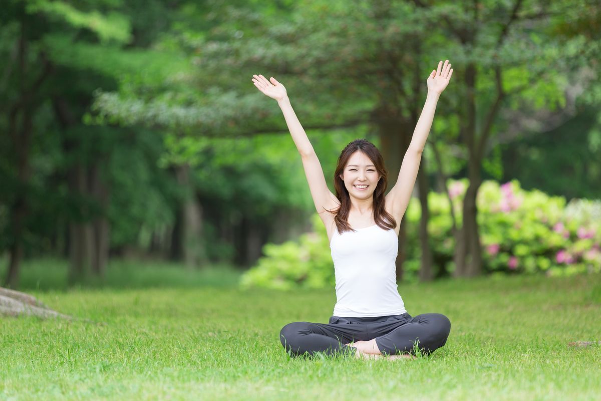Happy Asian woman sitting on the grass with her arms raised.