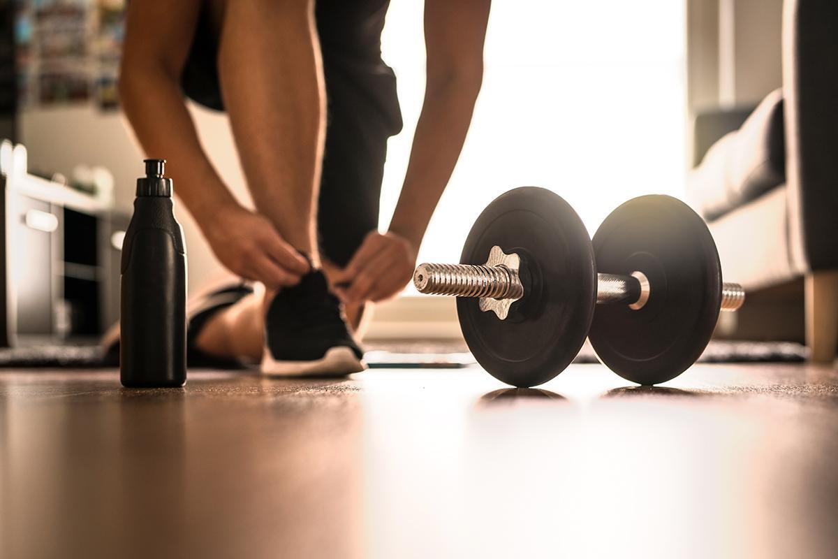 A man adjusts his shoe beside a dumbbell