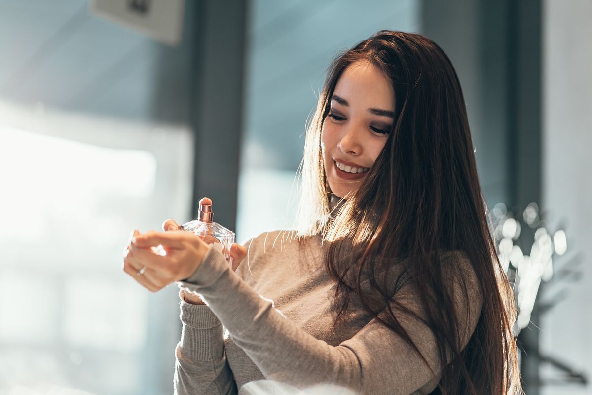 Asian woman with long hair spraying perfume on her wrist.