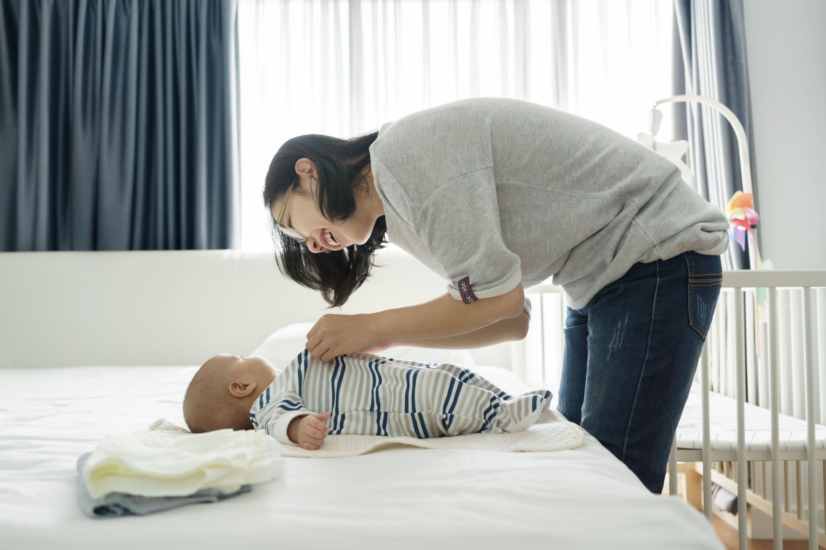 A woman dressing her baby on a bed