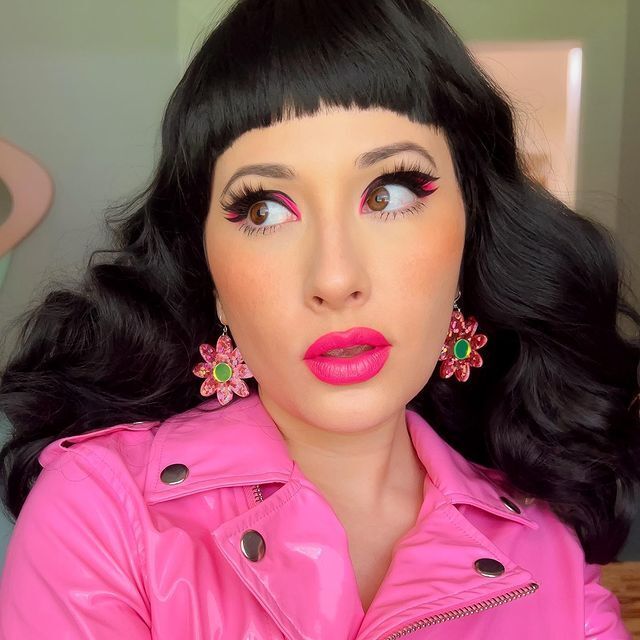 Woman with neon pink makeup wearing flower earrings and hot pink leather jacket.